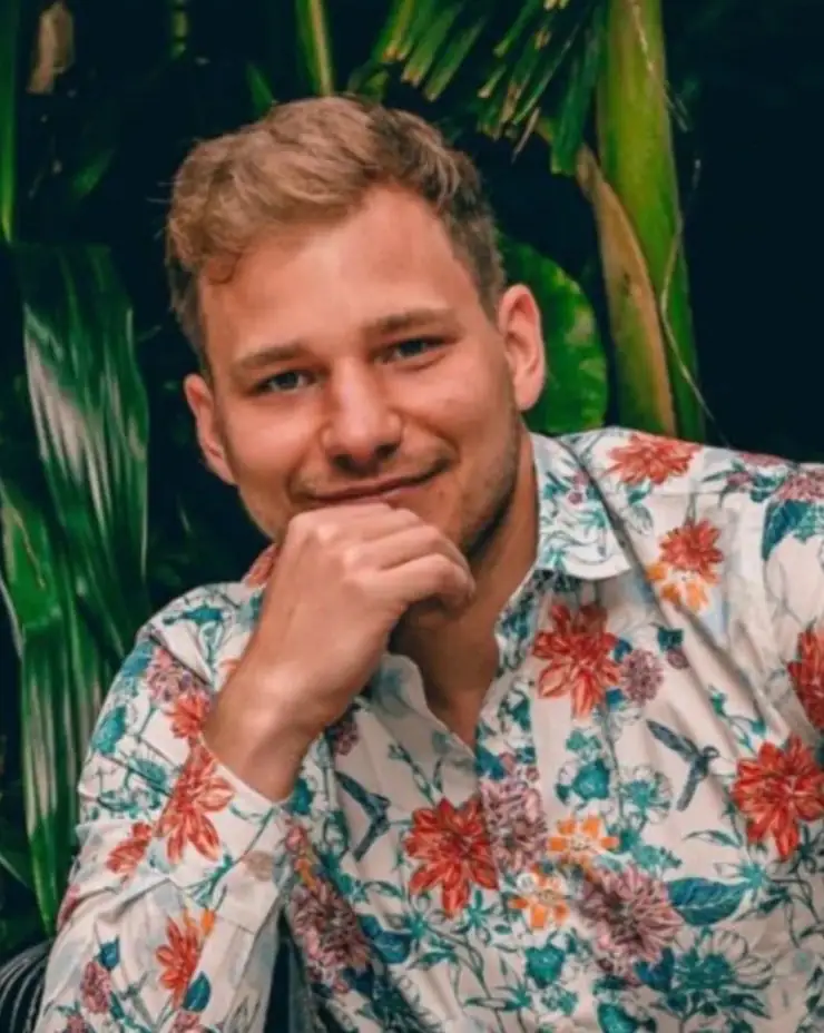 Oliver Glozik smiling, in a floral shirt in front of tropical leaves