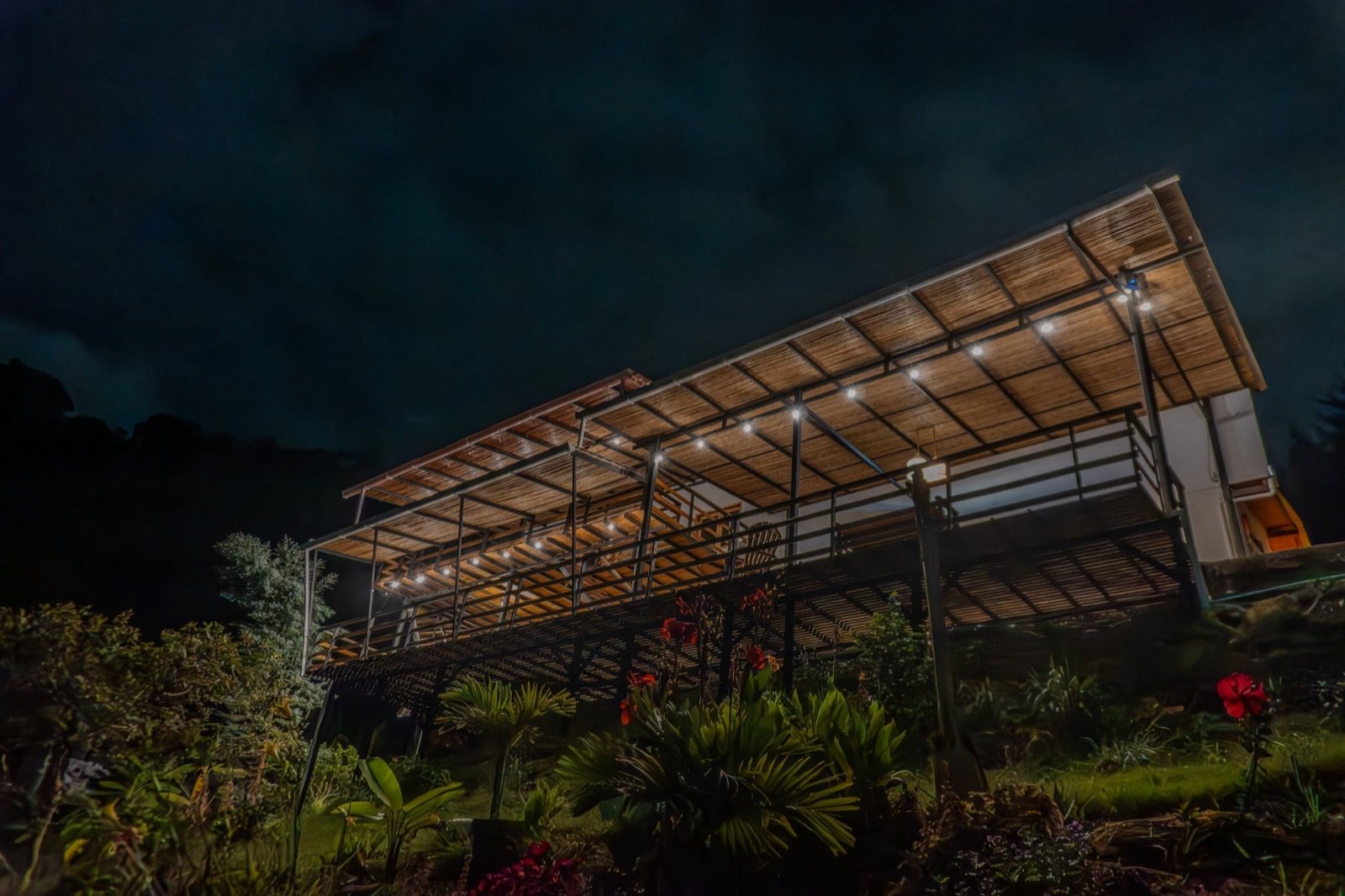 The retreat house at night, its long wooden deck lit by string lights above a tropical garden